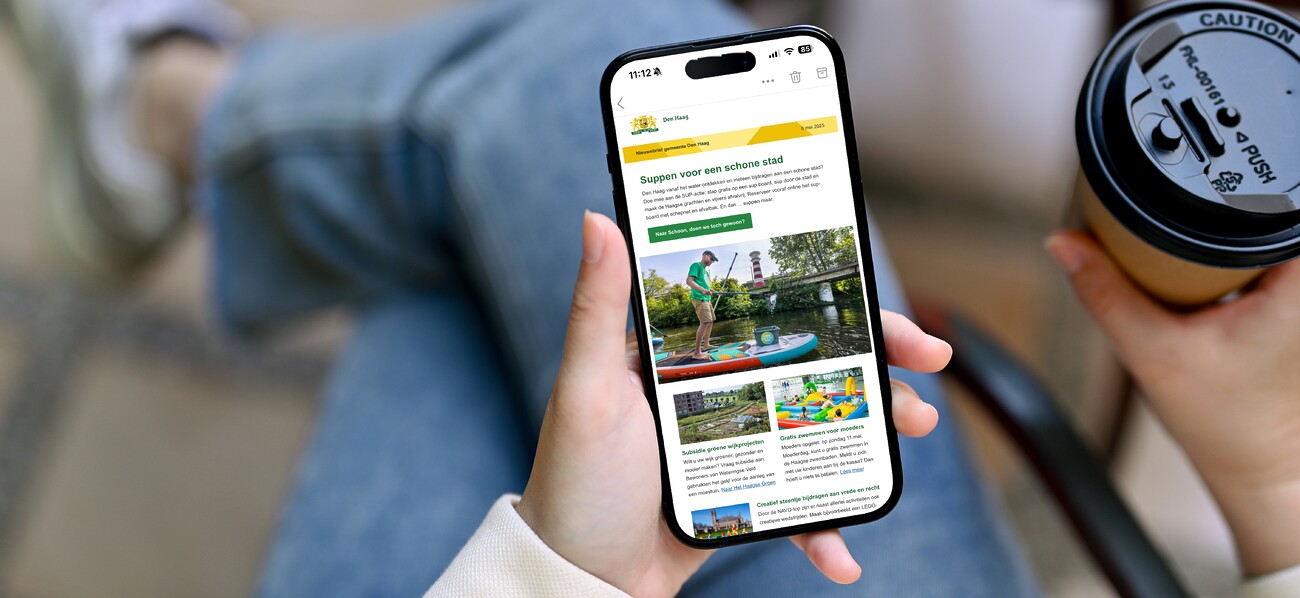 Vrouw houdt mobiele telefoon in hand met op het scherm de nieuwsbrief van de gemeente Den Haag.