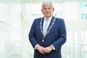 Portretfoto Jan van Zanen in donkerblauw pak, twee vingers in de linkerhand geklemd en met de ambtsketting om.