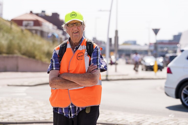 Boudewijn poseert op straat met de armen over elkaar en in neon oranje hes en neon gele pet.