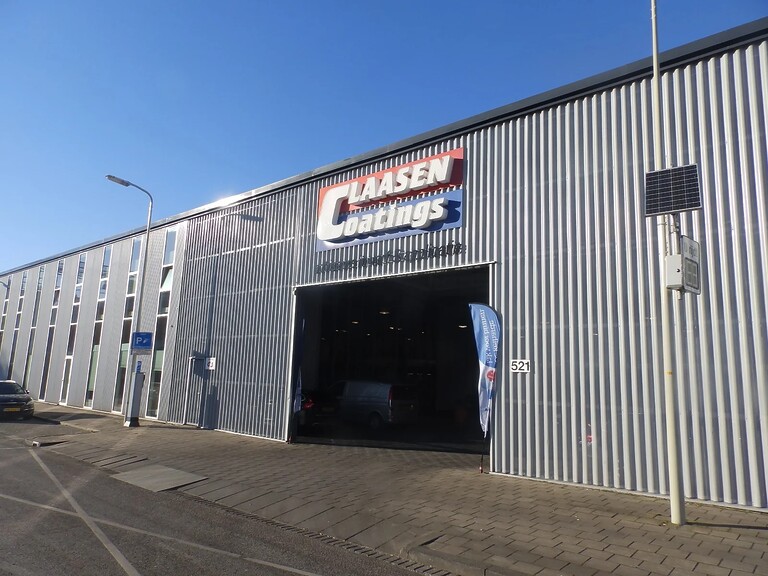 Gevel van het bedrijfspand van Claasen Coating: de muur lijkt van golfplaten, een logo in rood en blauw boven een grote garage-opening.
