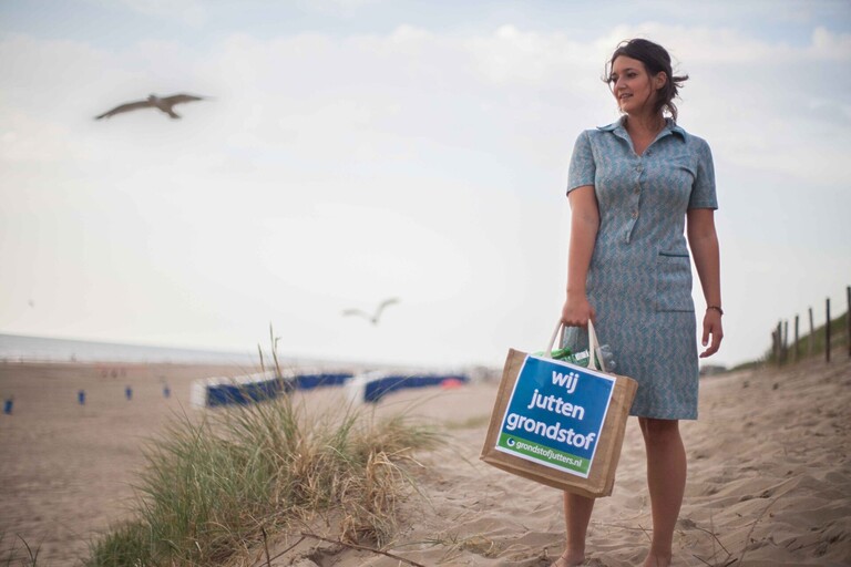 Noortje in lichtblauwe midi-jurk en juten tas op het strand