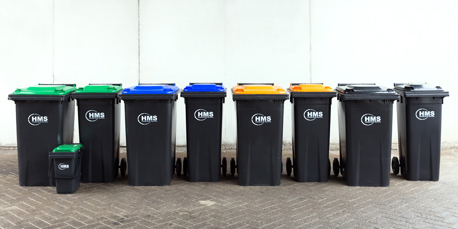9 vuilnisbakken op een rij. De bakken zijn donkergrijs en hebben een groene, blauwe, gele of grijze deksel.