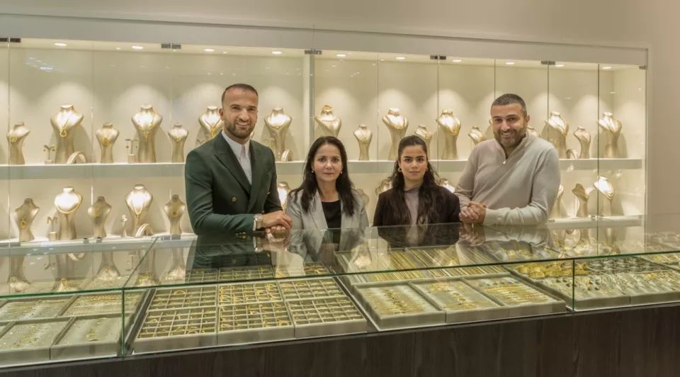 Zafer en Ahmet Yildiz flankeren 2 dames, een ouder, een jonger in de juwelierszaak. Ze leunen op een toonbank gevuld met gouden sieraden gesorteerd naar grootte.