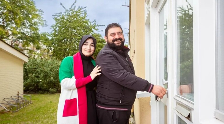 Ondernemers Selma Oruç en Burak Duman. Selma, met hoofddoek en wit, roze en groene overjas, leunt licht tegen de rug van haar man. Burak, in zwart, heeft een grote glimlach en steekt de sleutel in het slot van een deur, vermoedelijk van hun bedrijfspand.
