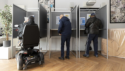 Kiezer zit in een stemhokje op een scootmobiel
