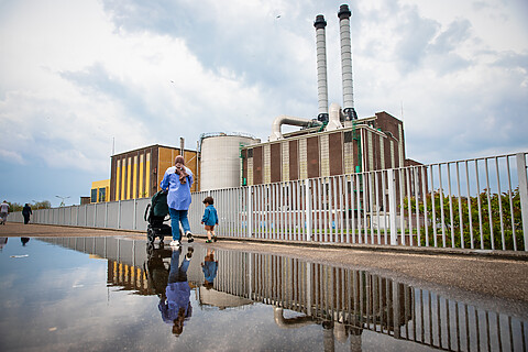 Een vrouw met kinderwagen en peuter loopt voorbij de energiecentrale.