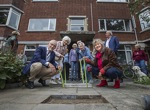 Een groepje buurtbewoners poseert met een te plaatsen nieuwe gulden klinker stoeptegel.