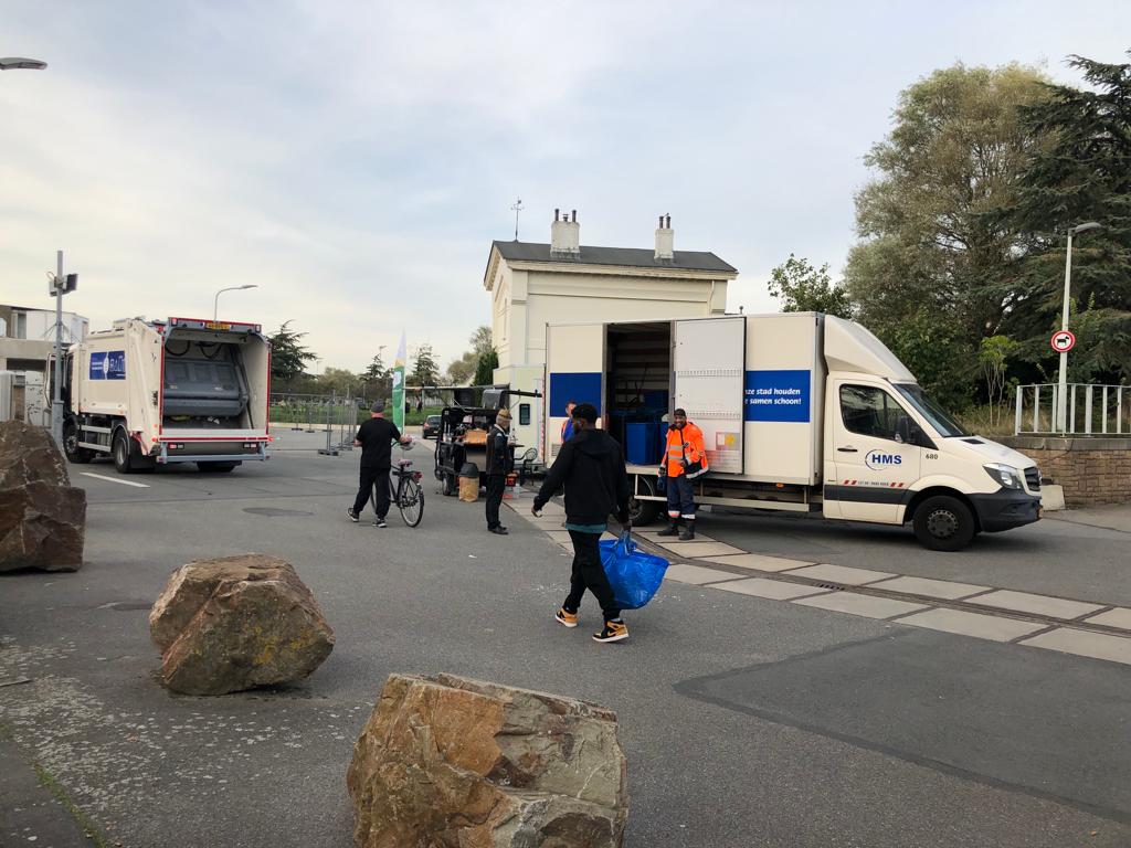Afbeelding van de Opruimdag waarbij mensen en afvalophalers afval verzamelen en inladen in vracthwagens.