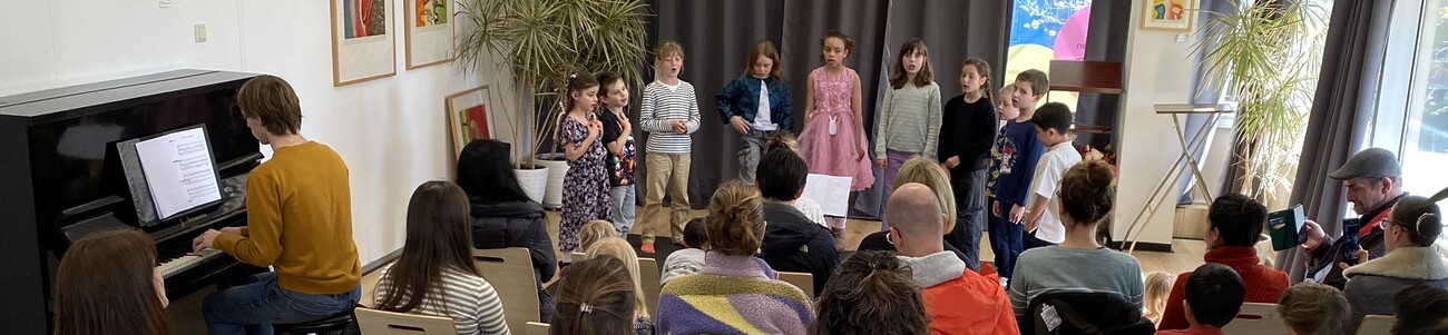 Kinderen zingen voor publiek en een man speelt piano