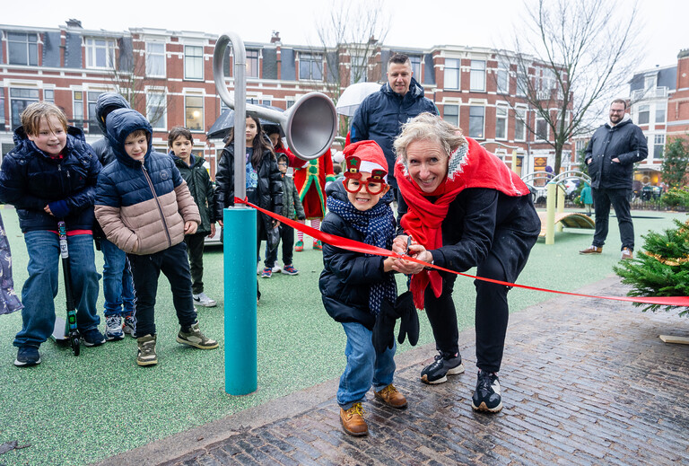 Stadsdeeldirecteur Mandy van Veen knipt samen met een kind een lintje door om de speeltuin op het Frederik Hendrikplein feestelijk te openen.