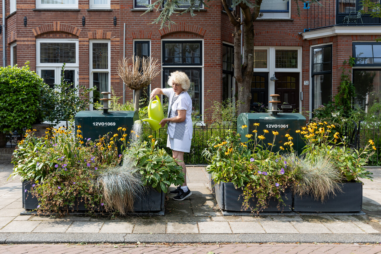 Den Haag, 19 augustus 2024 Een vrouw geeft de plantjes van het tuintje rondom een ORAC in de Marconistraat water.