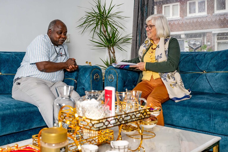 een energiecoach gezellig thuis op de bank in gesprek met een bewoner
