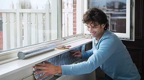 een man brengt isolerende folie aan achter de cv