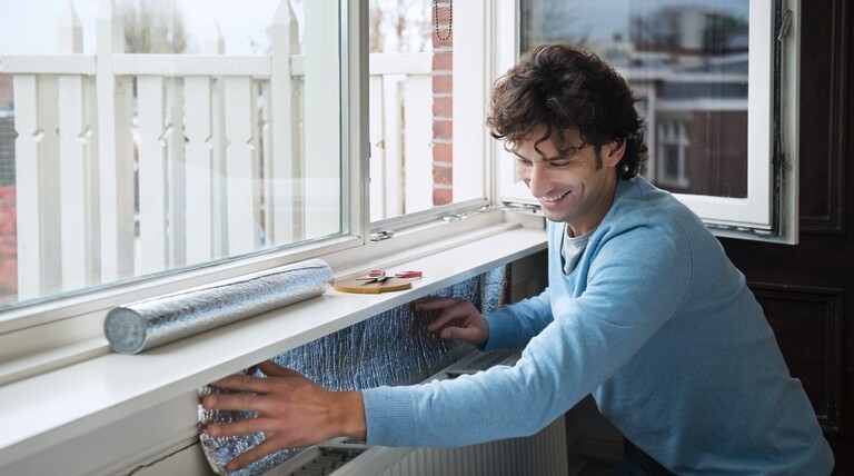 een man brengt isolerende folie aan achter de cv