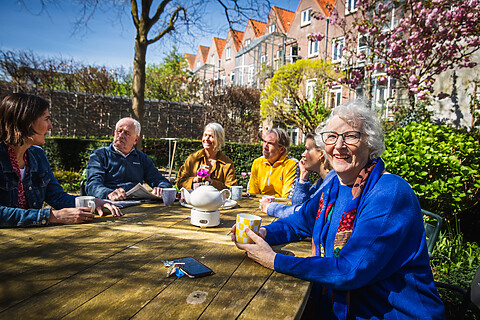Ouderen van een woongroep zitten buiten aan een tafel in de tuin.