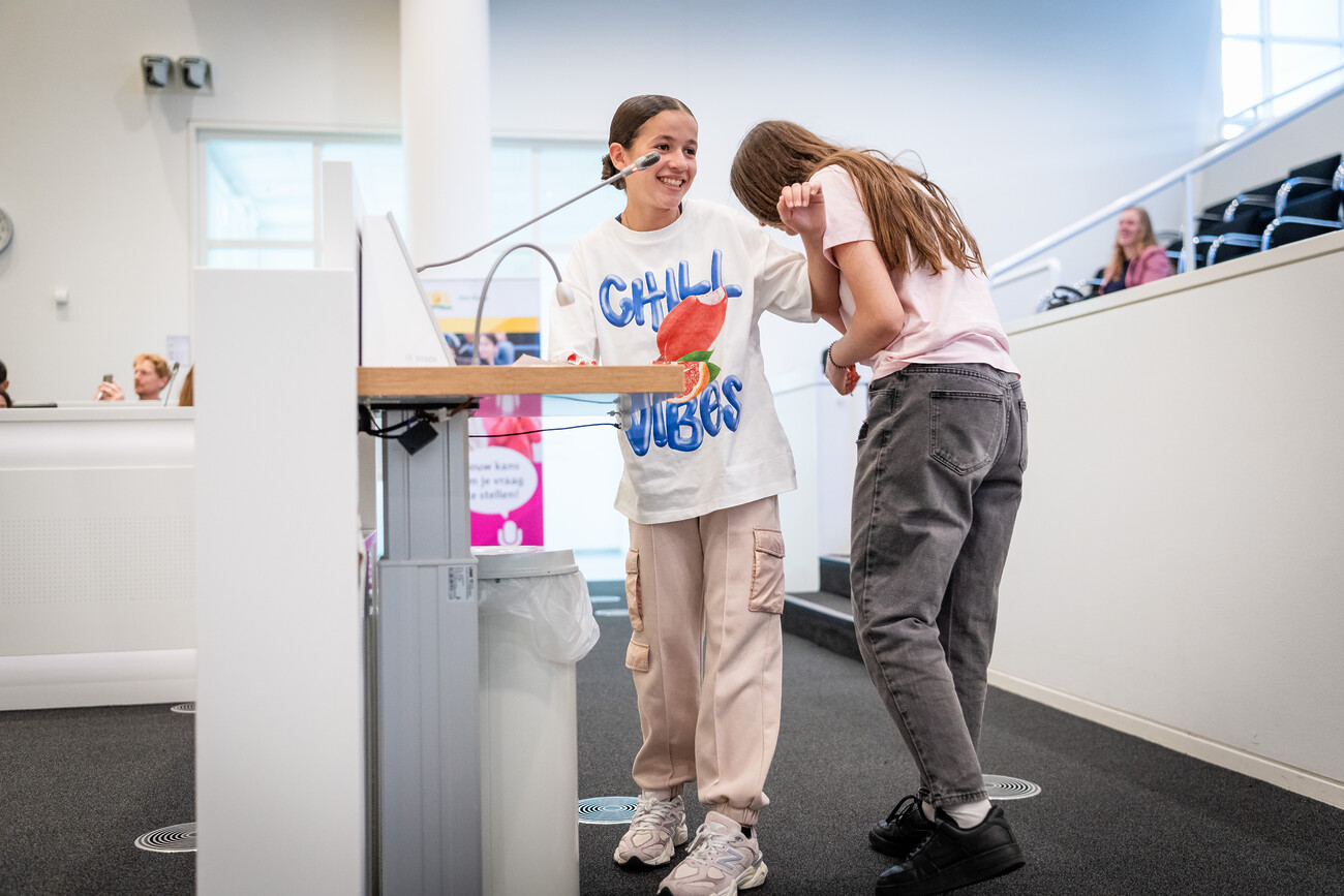 Twee leerlingen van praktijkschool De Einder staan te lachen achter de inspreekmicrofoon.