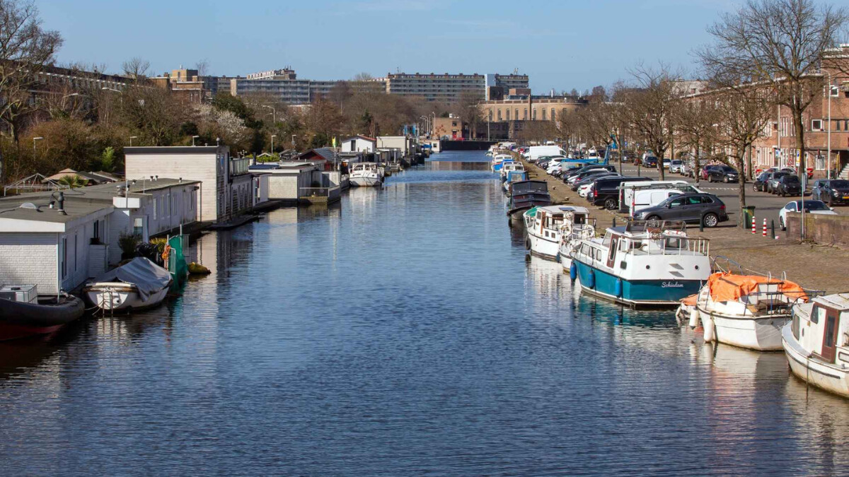 Kanaal in een zonnig Rustenburg-Oostbroek. Er liggen boten en woonboten langs de kant.