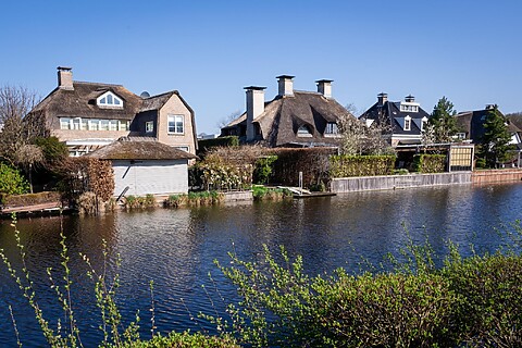 Grote huizen met rieten daken. Tuinen met veel planten. Liggen direct aan het water. Blauwe lucht en lentezon.