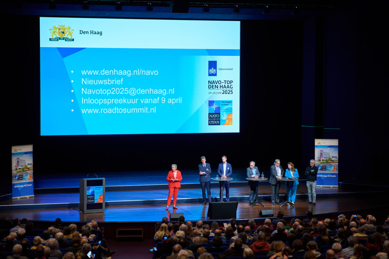 Informatiebijeenkomst NAVO-top. Een paar sprekers staan voor een scherm waarop een aantal betrouwbare communicatie middelen wordt genoemd.