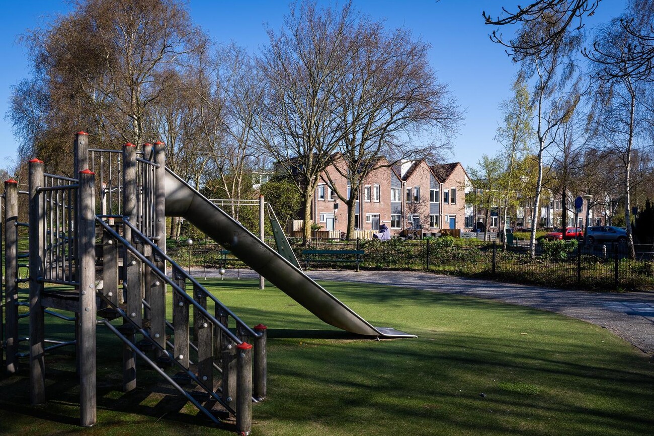 Speeltoestel met glijbaan op een groene speelplaats, omringd door bomen en een rustige woonwijk in Waldeck.