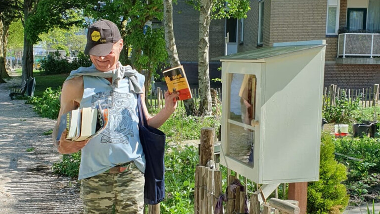 Jan-Willem bij de MiniBieb aan de Bontekoekade. Hij houdt verschillende boeken in zijn handen.