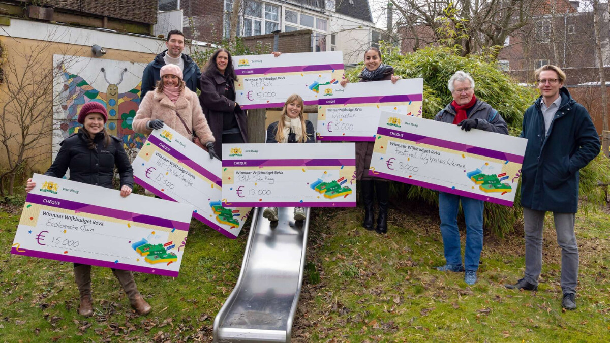 Foto van de winnaars van het wijkbudget Segbroek. Mensen staan met cheques in hun handen bij een glijbaan.