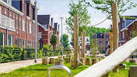 Speeltoestellen van hout tussen huizen. Touwen, boomstammen en palen. Groen gras. Rode bakstenen huizen op de achtergrond. Rustige woonstraat.
