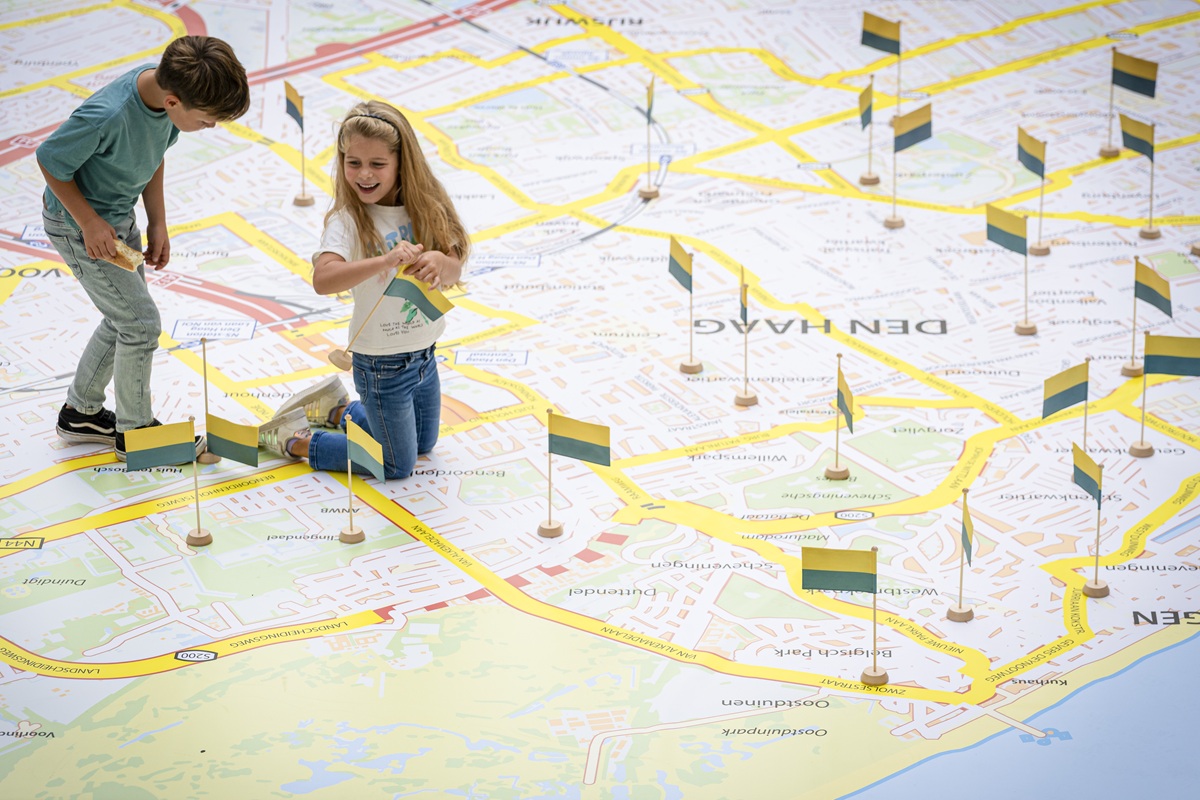 Twee kinderen zetten vlaggetjes neer op de plattegrond van Den Haag.