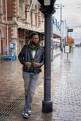 Een man leunt tegen lantaarnpaal op straat.