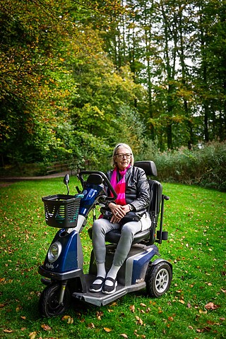 Vrouw zit op een scootmobiel in een park.