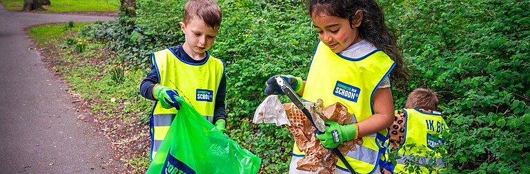 3 kinderen met gele hesjes rapen afvallen en stoppen het in een vuilniszak.