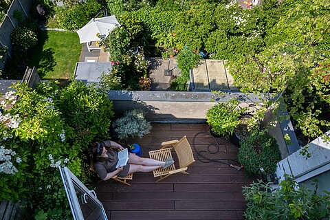 Vrouw leest in tuinstoel op haar dakterras met veel groen.