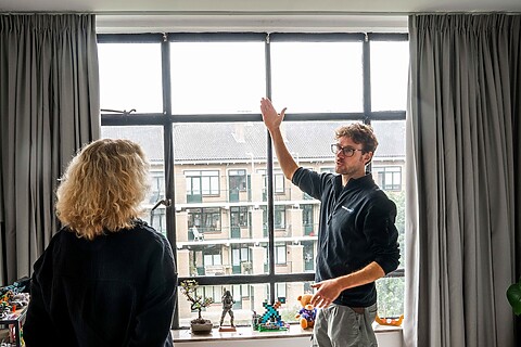 Een man staat voor een raam in een appartement en laat aan een vrouw het isolatieglas zien.