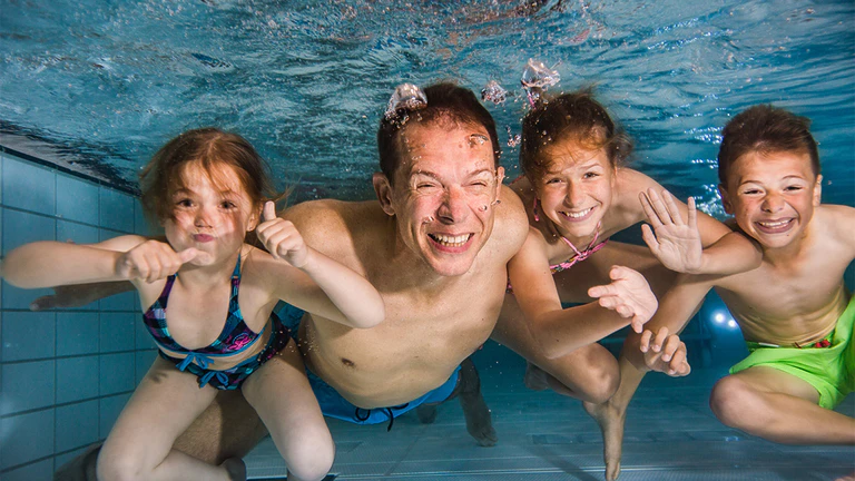 Vader en drie kinderen zwemmen samen onder water.