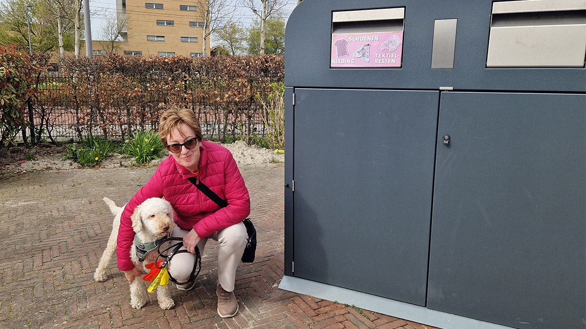 Vrouw met hond Drebbel naast een textielcontainer bij een stadsboerderij.
