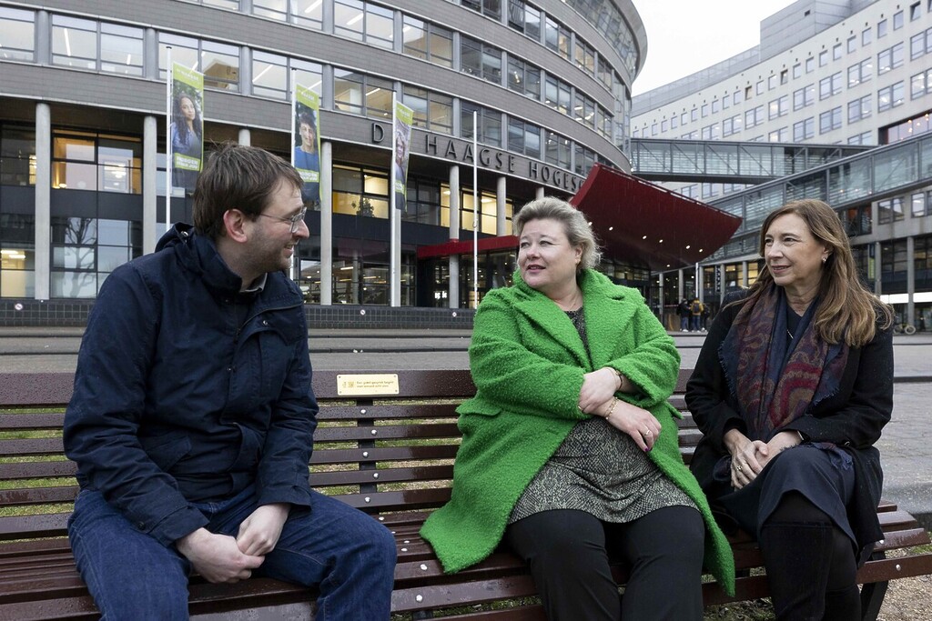 Three adults sitting on a bench in front of The Hague University
